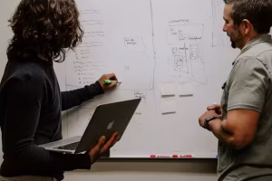 Two people talking strategy at a white board.