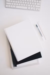 A blank notebook in front of a keyboard on a white table.